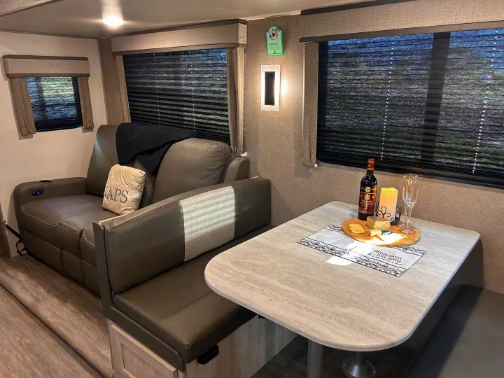 Cozy rv rental: sofa with "NAPS" pillow, inviting dinette table with wine & cheese, perfect for relaxing travels.. Forest River 26FKDS 2025