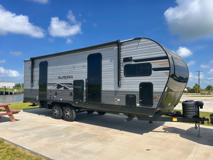 Spacious Aurora travel trailer RV rental parked at a sunny waterfront site, perfect for your next vacation.. Forest River 26FKDS 2025