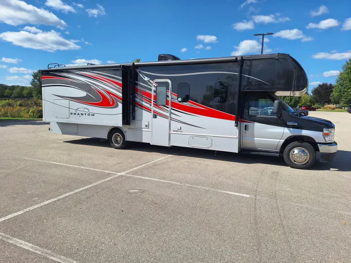 A striking black, gray, and red Class C Phantom RV rental, with slide-outs extended, is parked under a blue sky.. Nexus Phantom 2024