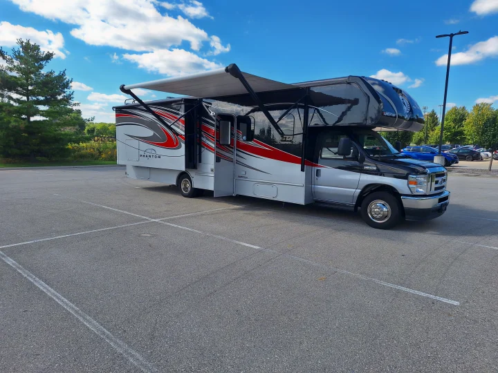 Large Class C RV rental, black & silver with awning extended, parked in a sunny lot. Perfect for travel adventures.. Nexus Phantom 2024