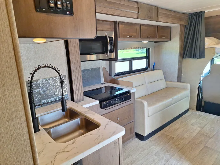 This RV rental's modern interior features a full kitchen with sink/stove, comfy sofa, and stylish wood-look flooring.. Nexus Phantom 2024
