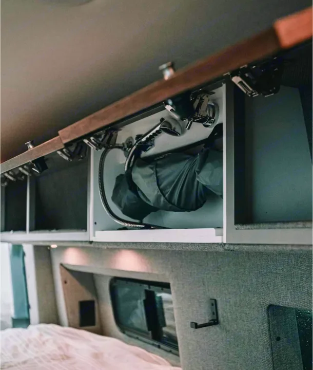 RV rental: Overhead cabinet reveals a compact stowed shower, hose, and storage, above a bed area.. Storyteller Overland Storyteller Overland Class B 2021
