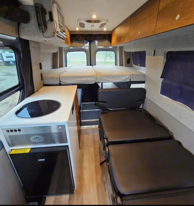 Inside this RV rental: a compact kitchen with stove/sink & fridge, rear convertible beds, and front passenger seating.. Storyteller Overland Storyteller Overland Class B 2021