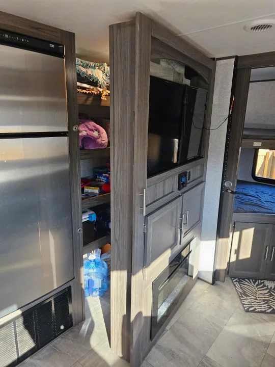 An RV rental's living area showcases a full-size fridge, open pantry, and built-in media center with a TV and fireplace.. Dutchmen Kodiak Ultra Lite 2021