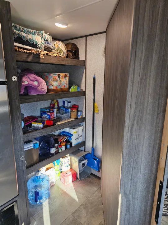 RV rental pantry: shelves packed with food, blankets, water, and cleaning supplies. Efficient storage.. Dutchmen Kodiak Ultra Lite 2021