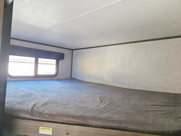 RV rental bunk bed interior with dark grey blanket, window, and textured walls.. Dutchmen Kodiak Ultra Lite 2021