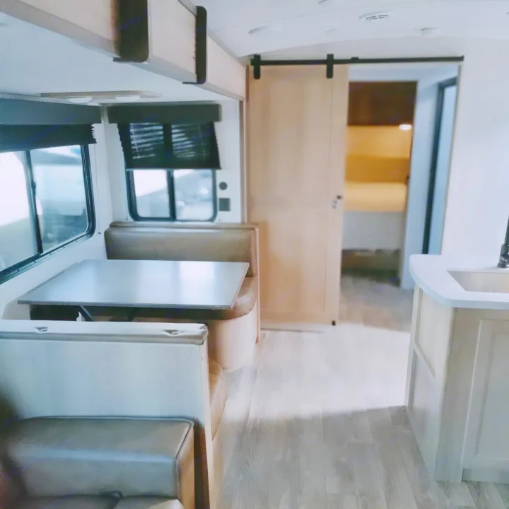Spacious RV rental interior featuring a dinette, compact kitchen, and a private bedroom accessible via a barn door.. Keystone RV Outback Ultra Lite 2024