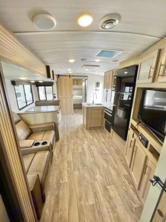 Spacious RV rental interior with modern living area, full kitchen, and a glimpse of the bedroom beyond.. Keystone RV Outback Ultra Lite 2024