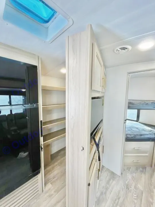 Inside a modern RV rental: skylight, wood-look cabinets, kitchen, pantry, and bunk beds in a light, clean style.. Keystone RV Outback Ultra Lite 2024