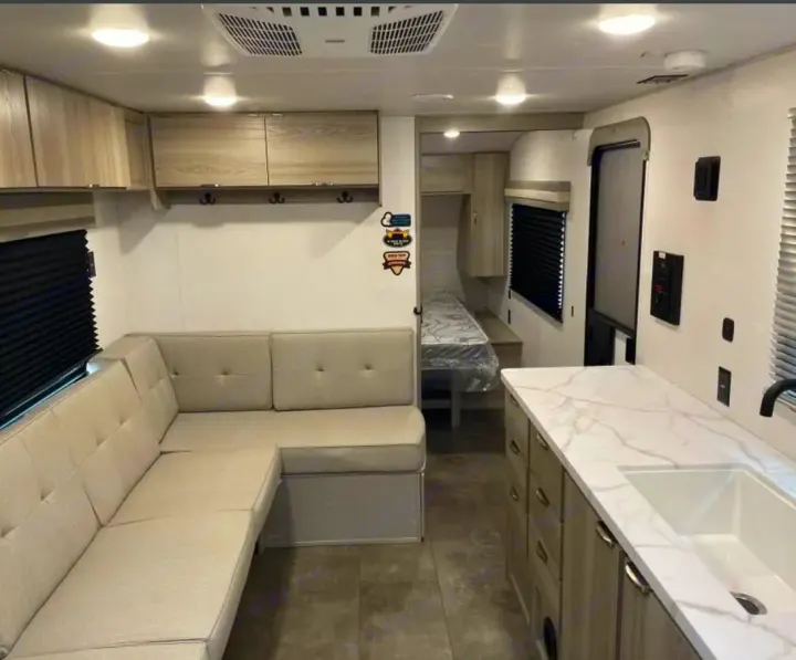 Clean, modern RV rental interior with an L-shaped sofa, kitchen counter, and sleeping area visible.. Forest River Salem Cruise Lite 2024