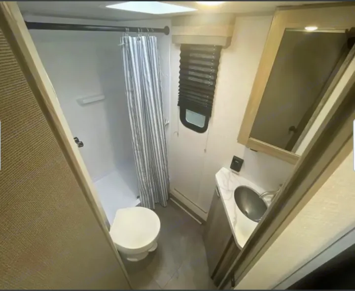 Inside an RV rental: Compact bathroom featuring a shower with striped curtain, toilet, and modern sink vanity.. Forest River Salem Cruise Lite 2024