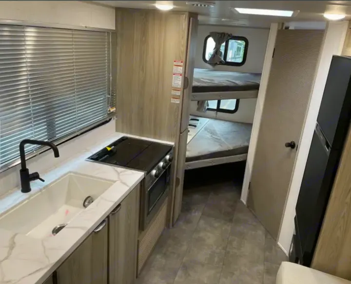 Modern RV rental interior features a functional kitchen with sink, stove, and built-in bunk beds for cozy sleeping.. Forest River Salem Cruise Lite 2024