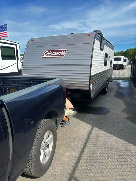Preparing an RV rental! A person connects a Coleman travel trailer to a pickup truck, with other RVs visible nearby.. Dutchmen Coleman 2024