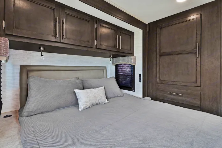 Experience comfort in this modern RV rental bedroom with gray bedding, built-in dark wood cabinets, and integrated lighting.. Jayco Redhawk SE 2024