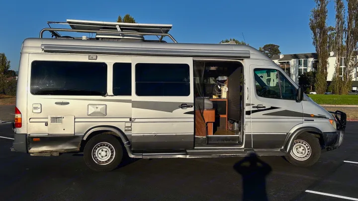 Silver Mercedes Sprinter RV rental parked outdoors, showing roof solar panels & open side door with interior view.. Airstream Interatate 2003