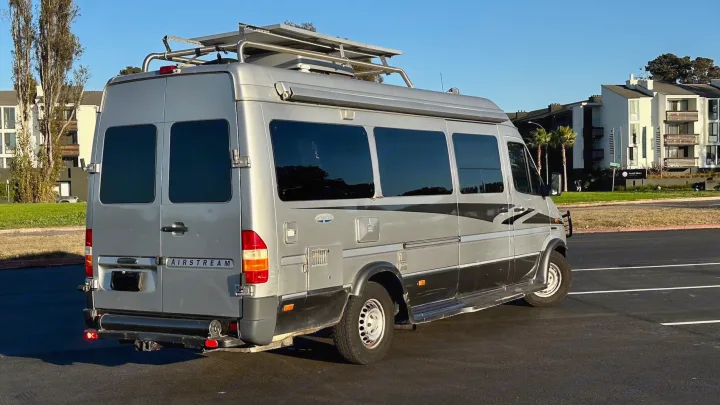 A silver Airstream Interstate van RV, ideal for an rv rental, showcasing its rear and roof rack with solar.. Airstream Interatate 2003