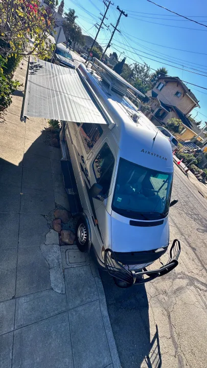 A silver Airstream RV rental van with awning extended, parked on a sunny street. Your next adventure awaits!. Airstream Interatate 2003