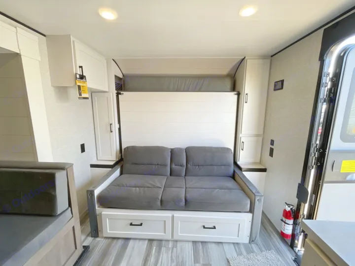 An RV rental's bright interior features a grey sofa that converts to a murphy bed, white cabinets, and an open entry door.. Jayco Jay Flight SLX Baja Edition 2025