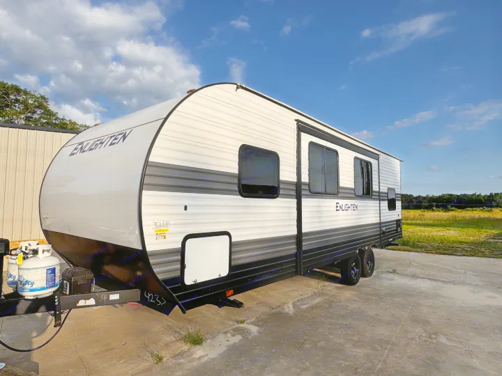A new white & grey "Enlighten" travel trailer is parked on concrete, ideal for your next rv rental or camping trip.. Gulf Stream Enlighten 2025