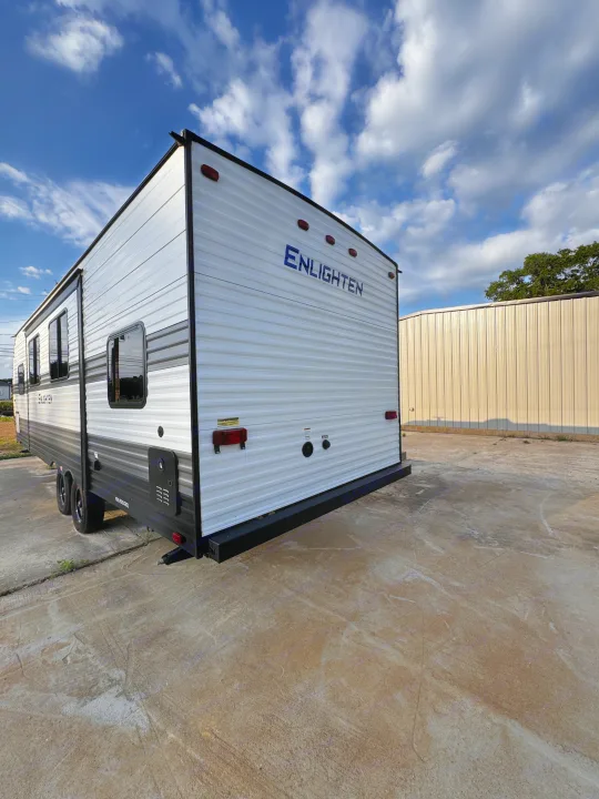 White & gray ENLIGHTEN travel trailer parked on concrete lot under blue sky with clouds. Ideal for RV rental.. Gulf Stream Enlighten 2025