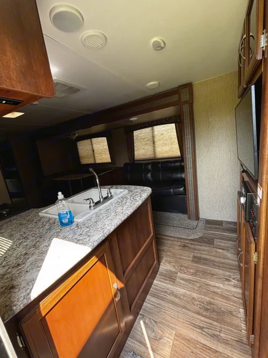 Bright RV rental interior with granite-look counter, sink, U-shaped seating, and entertainment unit. Wood-style floor.. Keystone RV Passport Grand Touring 2016