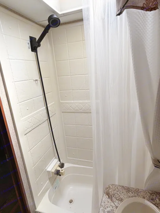 View of a compact RV rental bathroom with a white shower and tub unit, featuring a black shower head, fixtures, and curtain.. Keystone RV Passport Grand Touring 2016