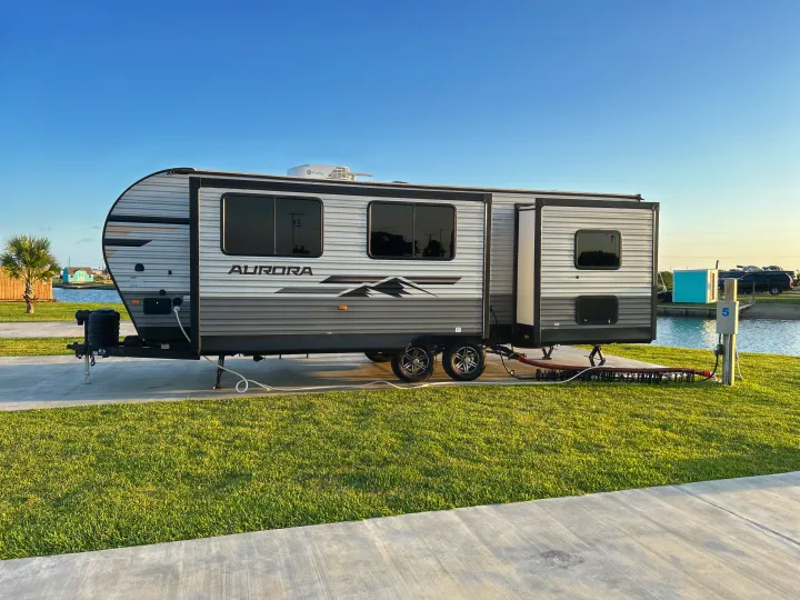 Spacious Aurora RV rental parked at a serene waterside campsite with lush green grass and concrete pad.. Forest River 26FKDS 2025