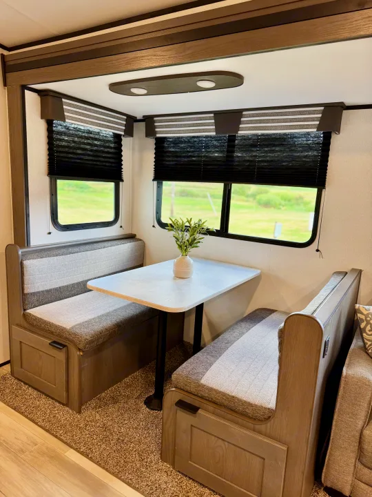 Cozy RV rental dinette with comfortable bench seating, a table, and bright windows revealing green outdoor views.. Cruiser RV MPG Ultra Lite 2022
