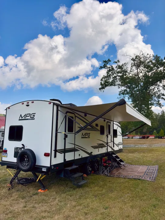 White MPG travel trailer rv rental with awning extended, set up in a green campsite under a blue sky with fluffy clouds.. Cruiser RV MPG Ultra Lite 2022