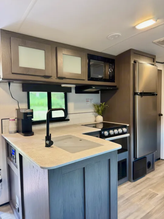 Inside a modern rv rental, this kitchen has grey cabinets, stainless appliances, a sink, and Keurig machine. A bright, functional space.. Cruiser RV MPG Ultra Lite 2022