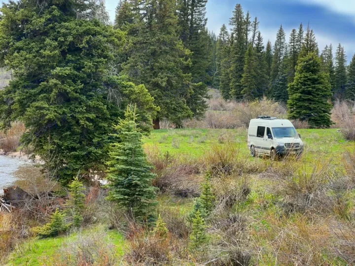 White camper van, perfect for an rv rental adventure, parked in a lush forest clearing near a river.. Mercedes-Benz Sprinter 2019