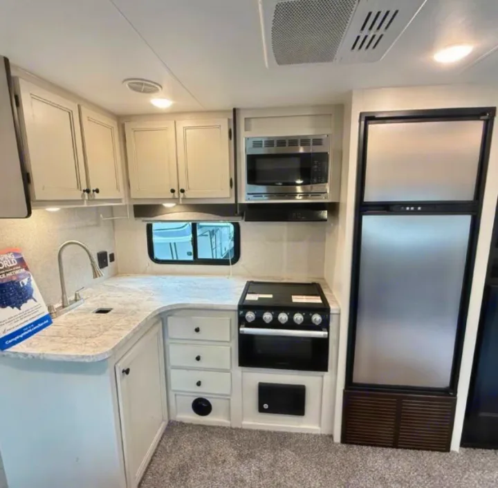 Inside an RV rental: a bright, functional kitchen with modern white cabinetry, stainless appliances, and sink.. Highland Ridge RV Range Lite 2021