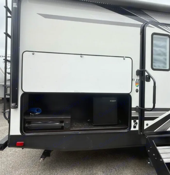 This RV rental features an open side storage bay revealing an outdoor kitchen setup with a pull-out griddle and a portable fridge.. Highland Ridge RV Range Lite 2021