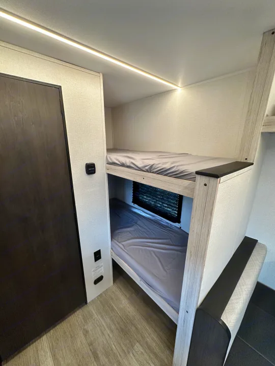 RV rental bunk beds: a clean, modern interior with top bunk LED lighting, a lower bunk window, and wood-look flooring.. Heartland Mallard 2025
