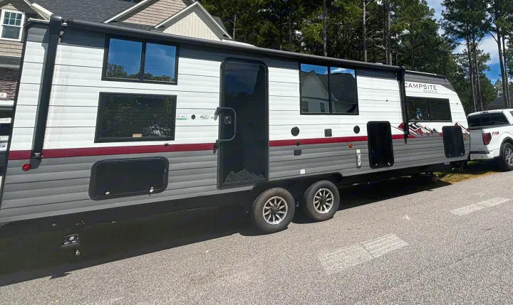 An RV rental: a large "Campsite Reserve" travel trailer, white and grey, hitched to a white pickup truck, parked on asphalt.. Forest River Campsite Reserve 23LM 2024