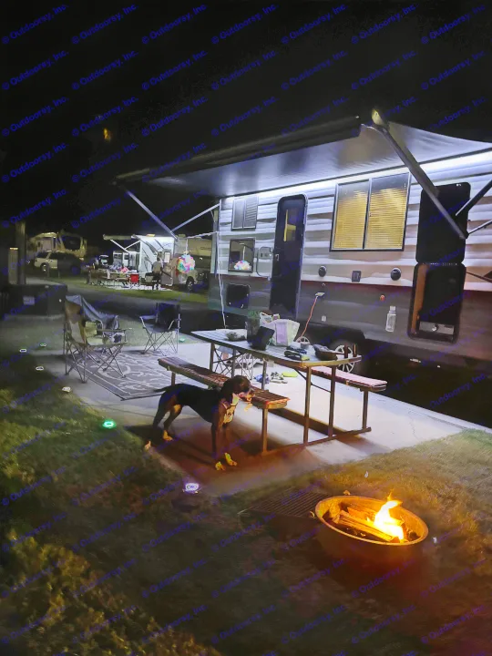 Cozy RV rental camping setup at night. A dog, illuminated RV, picnic table, and a warm fire pit create a perfect scene.. Forest River Campsite Reserve 23LM 2024