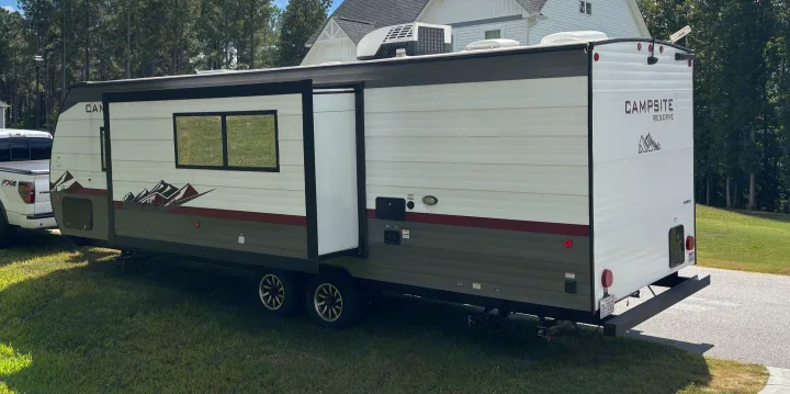 White and green RV rental (travel trailer) with extended slide-out, parked on grass. Ideal for camping & outdoor adventures.. Forest River Campsite Reserve 23LM 2024