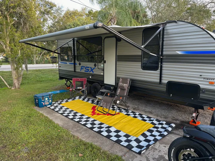 Relaxing outdoors with an RV rental featuring an extended awning, chairs, cooler, and motorcycle on a checkered mat.. Forest River Salem 2021