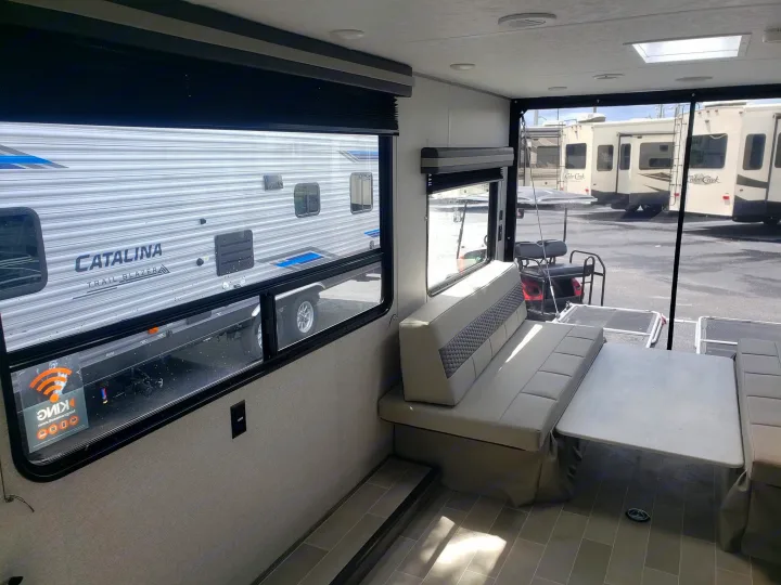 Interior of an RV rental: a modern living space with light-colored dinette seating, table, and large windows revealing other RVs outside.. Forest River Salem 2021