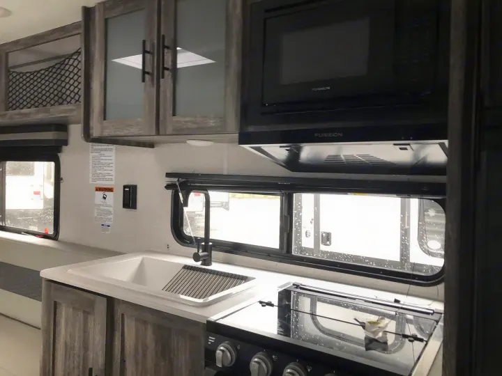 Spacious RV rental kitchen with modern light countertops, wood-grain cabinets, a sink, stove, and microwave.. Forest River Salem 2021