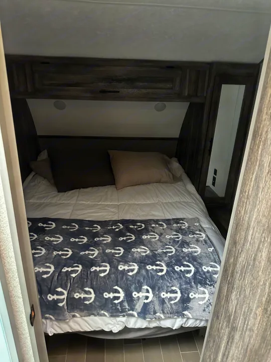 Cozy RV rental bedroom with white bedding, a gray anchor blanket, dark wood-look cabinetry, and overhead lighting.. Forest River Salem 2021