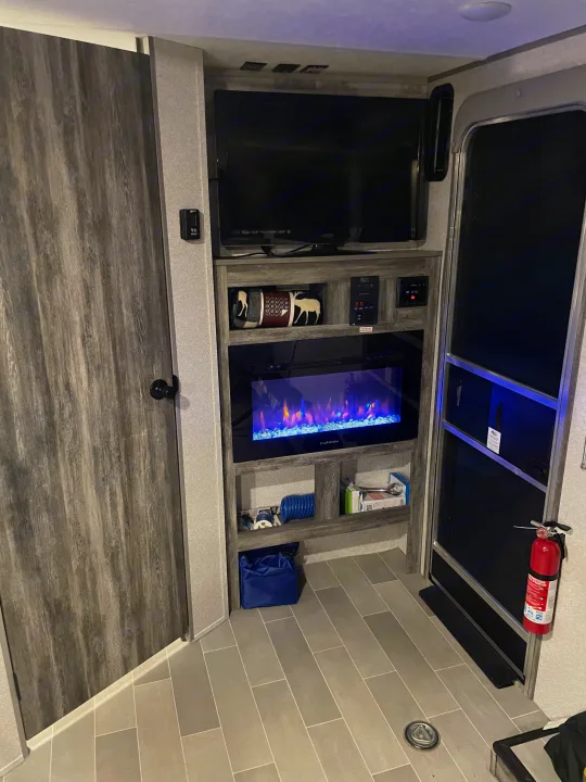 Modern rv rental interior with an entertainment center featuring a Vizio TV, illuminated electric fireplace, control panels, and storage.. Forest River Salem 2021