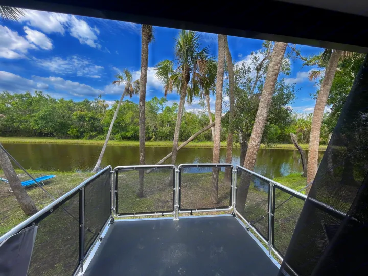 This RV rental offers a spacious deck with mesh railings, providing a scenic view of a tranquil pond, palm trees, and a blue sky.. Forest River Salem 2021