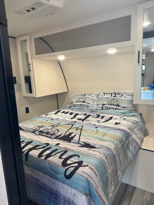 Cozy rv rental bedroom: A bed with "Happy Camping" bedding, shiplap wall, overhead storage, and AC unit. Ideal for travel!. Jayco Jay Jay Flight 294QBS 2025