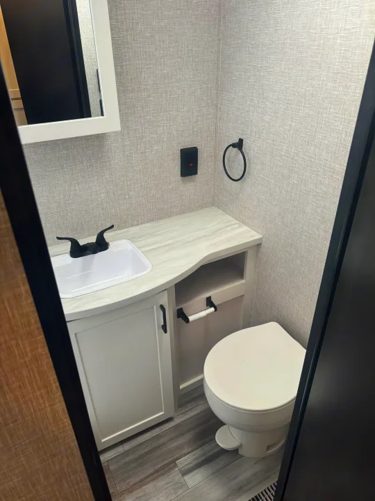 Inside a clean RV rental bathroom: white sink, toilet, and vanity against grey textured walls and wood-look floor.. Jayco Jay Jay Flight 294QBS 2025