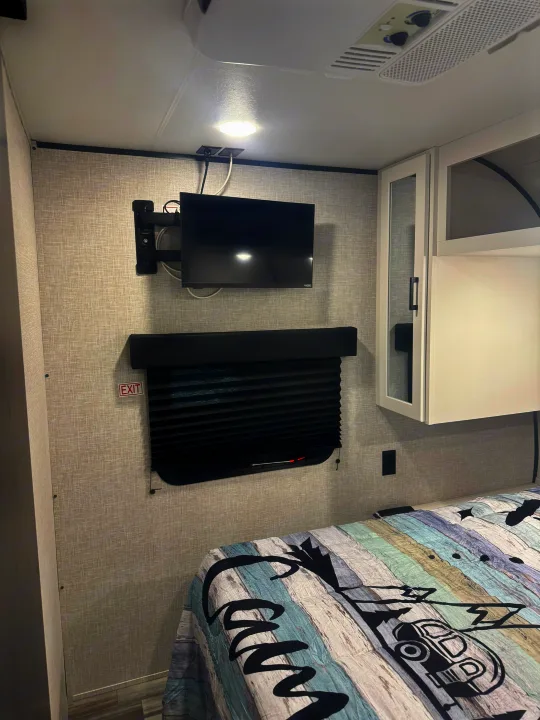 Cozy RV rental bedroom with TV, window, bed featuring a camping comforter, and overhead storage cabinets.. Jayco Jay Jay Flight 294QBS 2025