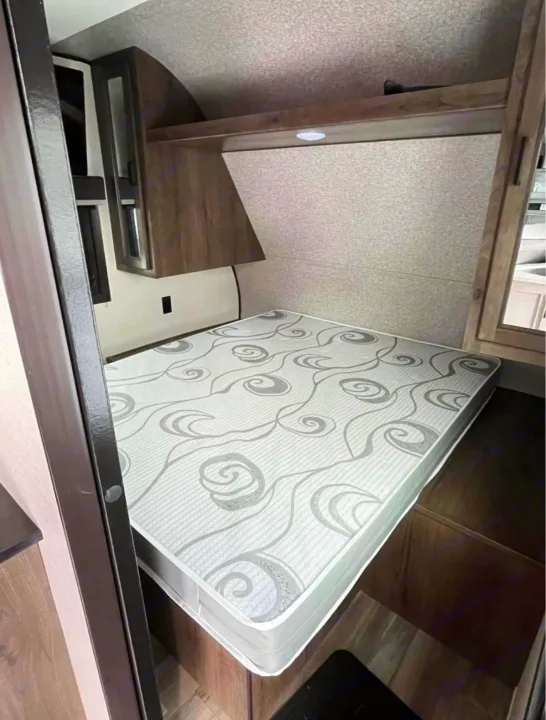 RV rental sleeping area with a patterned mattress, wooden overhead storage, and integrated lighting. Cozy and compact for travel.. Highland Ridge RV Open Range 2022