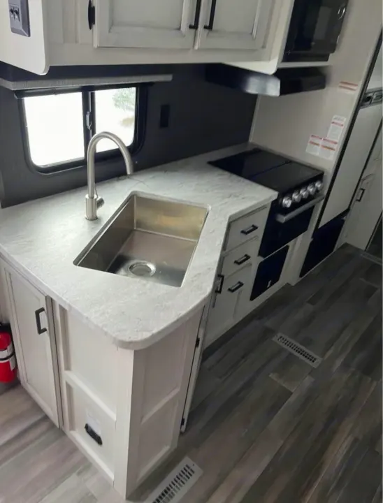 Interior of an RV rental: a clean, functional kitchen with a stainless steel sink, stove, microwave, and ample counter space.. Highland Ridge RV Open Range 2022