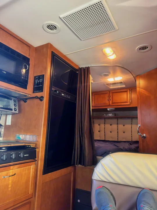 Cozy rv rental interior with compact kitchen appliances, a refrigerator, and a glimpse into the separated bedroom area.. Winnebago Minnie Winnie 2019
