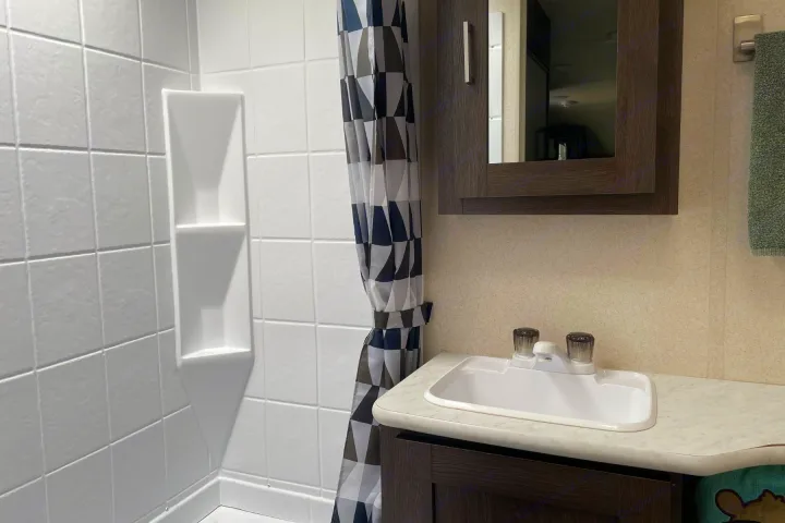 RV rental bathroom with a white tiled shower, geometric curtain, and compact vanity with sink and mirror. Perfect for travel.. Forest River Wildwood X-Lite 2018